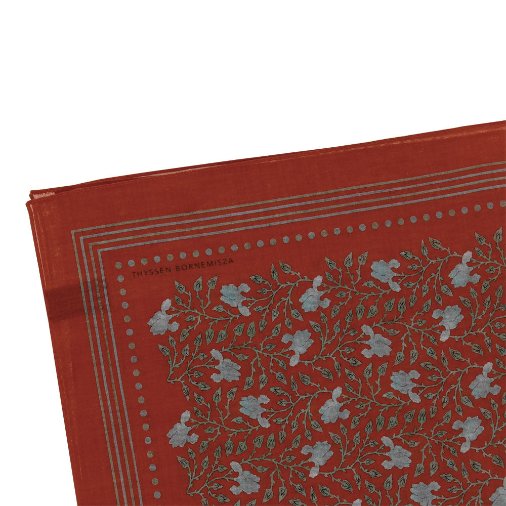 esquina de pañuelo estampado con flores verdes sobre fondo rojo enmarcado.